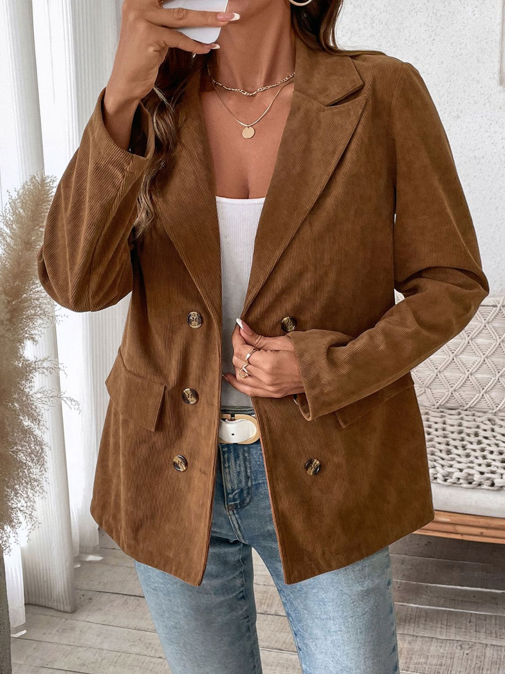 A woman wearing a brown corduroy double-breasted blazer with flap pockets and a lapel collar.