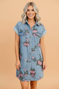 A light blue floral denim shift dress with rolled short sleeves and a buttoned front closure.