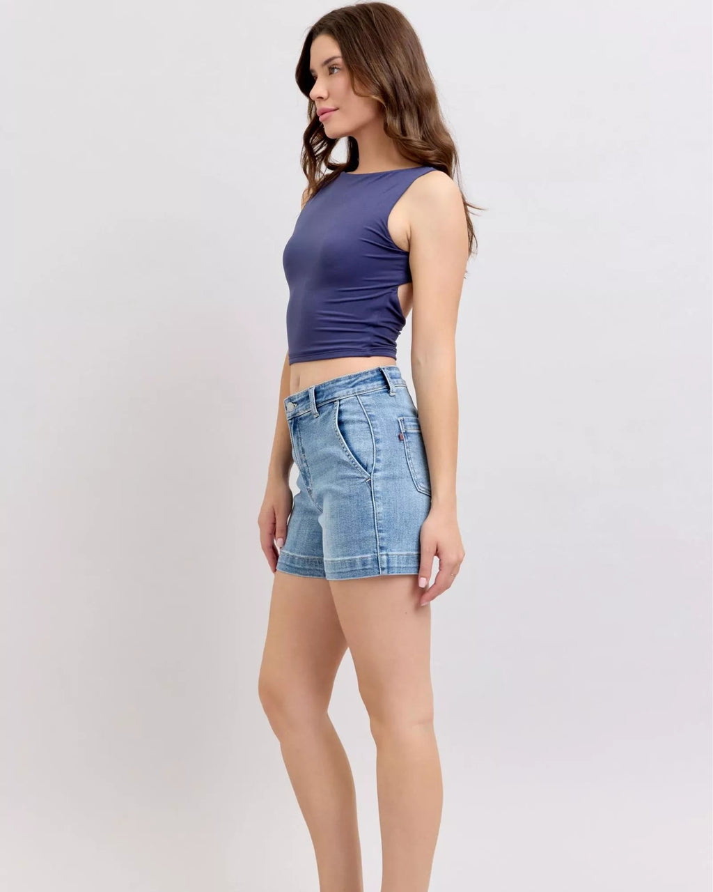 Woman wearing a purple sleeveless top and blue denim shorts on a white background