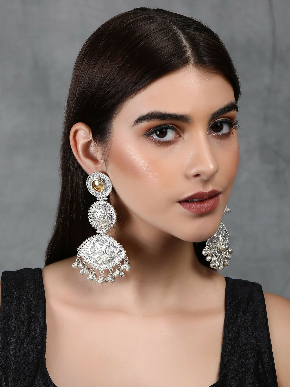 Close up of handcrafted silver tone earrings featuring intricate patterns and sparkling stone accents.