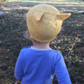 A bright yellow handmade knit baby beanie with adorable kitten ears, displayed in a sunny, whimsical lifestyle setting.