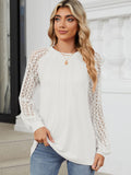 A woman wearing a long-sleeve white top with intricate lace sleeves and a round neckline.