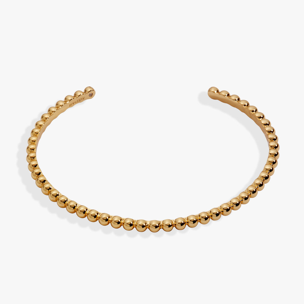 Gold beaded textured cuff bracelet worn on a wrist, featuring a light-catching design.
