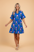 A woman wearing a bright blue mini dress with a pink floral pattern, V-neck, and tiered skirt.