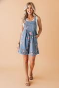 A woman modeling a blue denim romper with a pink and green floral print, featuring adjustable straps and pockets.
