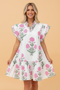 A woman wearing a white mini dress with a pink and green floral print, scalloped V-neck, and flutter sleeves.