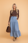Model wearing a light blue tiered denim maxi skirt with an elastic waistband and side pockets.