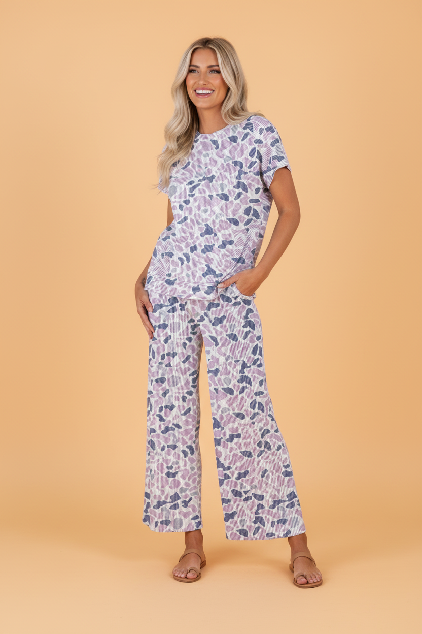 Model wearing a purple and white camo print two-piece corded knit set with short sleeves and wide-leg drawstring pants.
