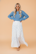 A tiered white maxi skirt with small blue floral patterns, styled with a blue sweater.