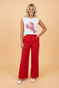 Woman wearing a white sleeveless knit sweater tank with a red gingham crawfish graphic, paired with red wide-leg trousers.