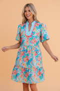 Woman wearing a floral stripe mini dress with teal, pink, and orange patterns and scallop trim.