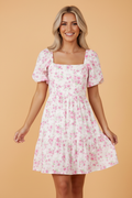 Front view of a white mini dress with pink floral print, square neckline, puff sleeves, and a tie-back detail.