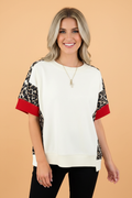 Woman wearing a white, red, and leopard-print patchwork knit top with an uneven hem.