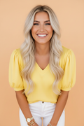 A woman wearing a vibrant yellow short puff sleeve V-neck blouse in a casual setting