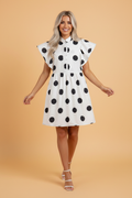 Model wearing a black and white polka dot mini dress with ruffled sleeves, shirt collar, and half-button placket.