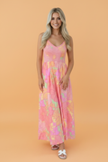 A woman wearing a vibrant floral print spaghetti strap dress with a shirred high waist and pockets.