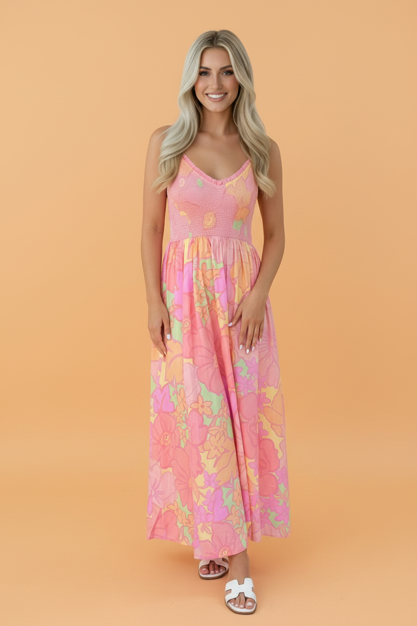 A woman wearing a vibrant floral print spaghetti strap dress with a shirred high waist and pockets.