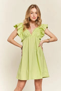 Woman wearing a lime green smocked back ruffled cap sleeve babydoll dress in a summer setting