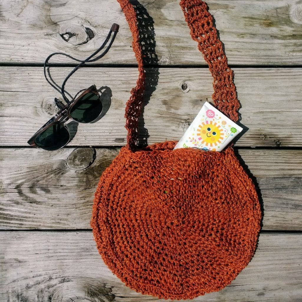 Bohemian circular crochet bag in rust and terracotta sitting on a beach