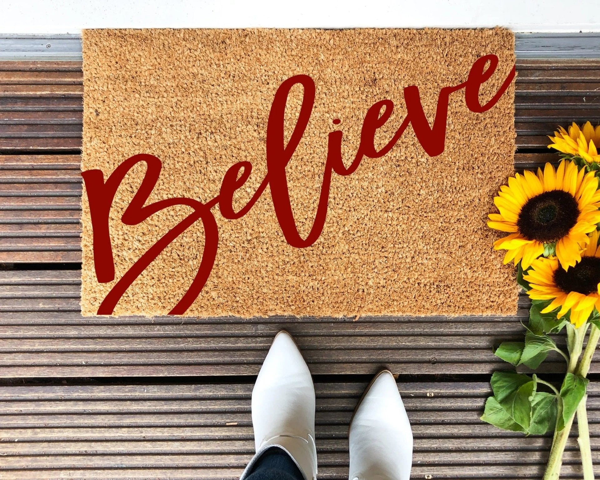 Rustic Believe holiday doormat with red script on natural coir at an outdoor entryway.