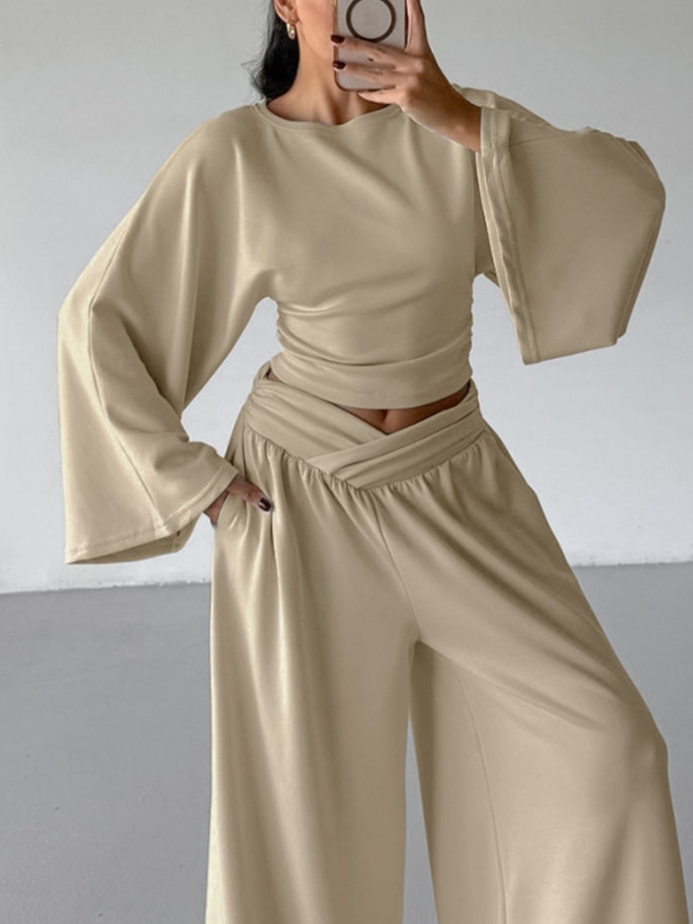 Person wearing a beige outfit with wide sleeves and high-waisted pants against a plain background
