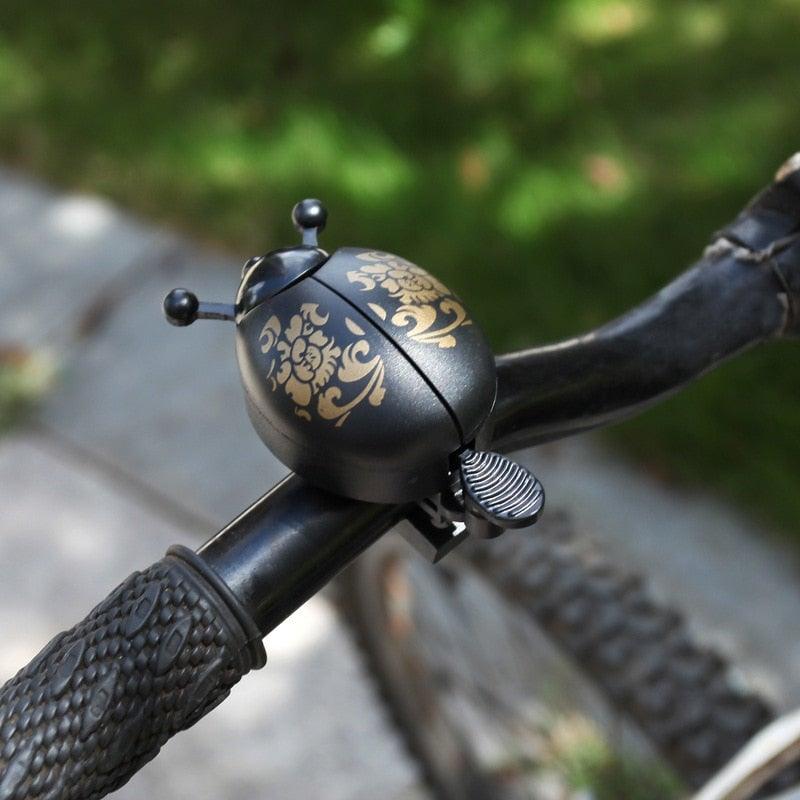 Stylish ladybug-themed metal bicycle bell mounted on a sleek bicycle handlebar.