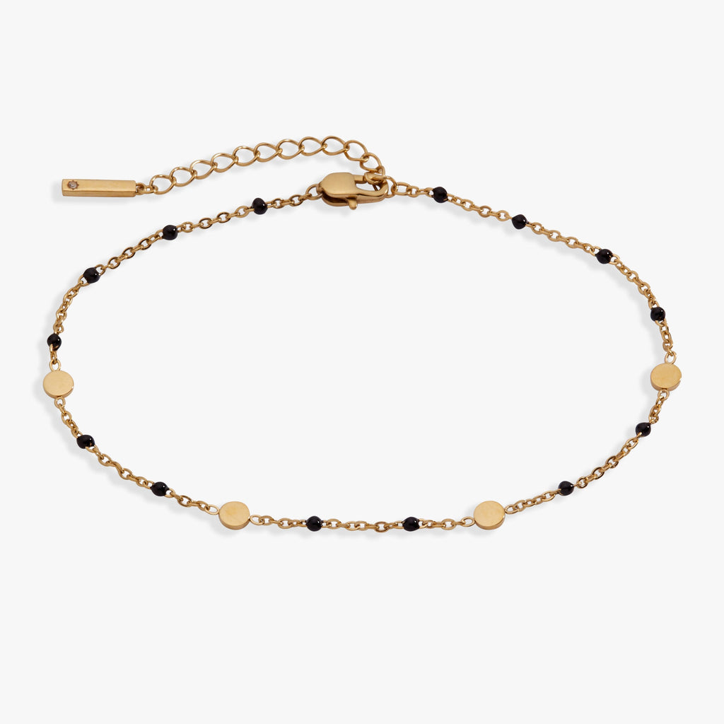 Gold-plated anklet featuring bold black enamel coin stations for charm personalization