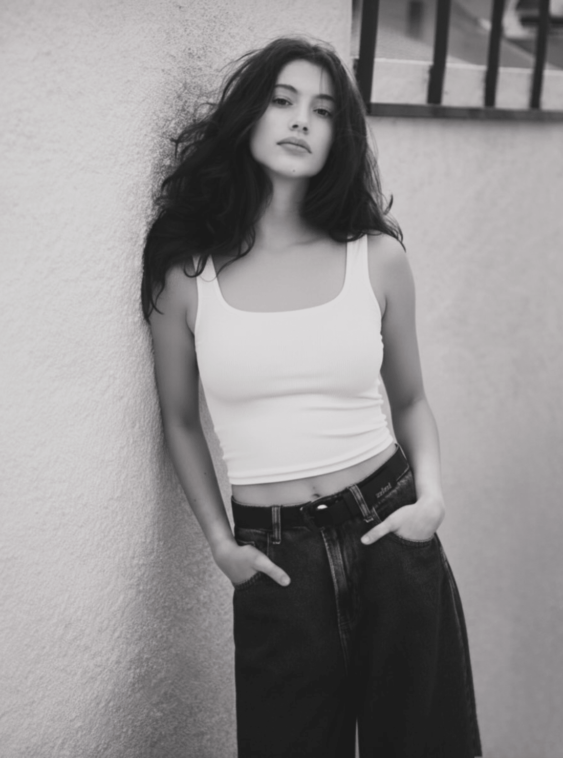 A woman wearing a white ribbed scoop neck tank top paired with blue jeans.