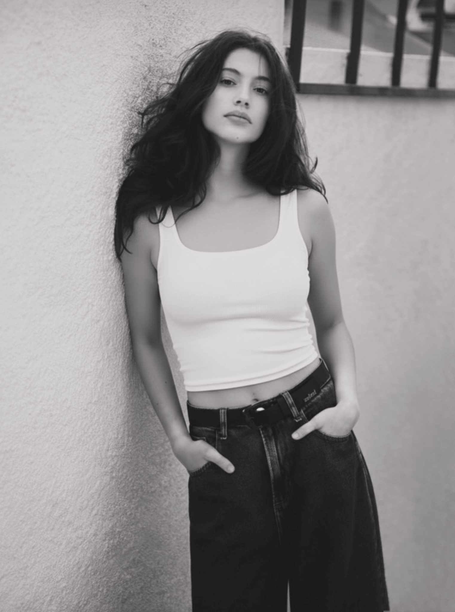 A woman wearing a white ribbed scoop neck tank top paired with blue jeans.
