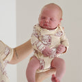 A newborn baby wearing a cream-colored long-sleeve snapsuit with a red milk carton print.