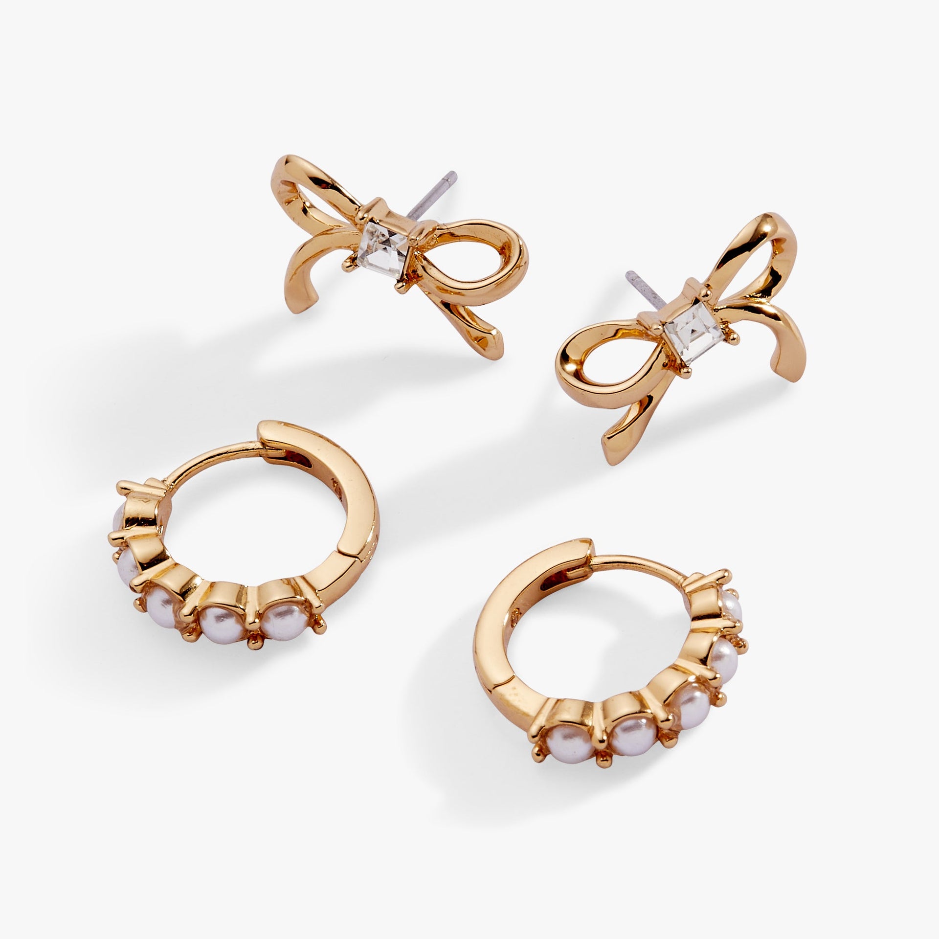 A set of gold-plated bow studs and white pearl huggie hoop earrings displayed elegantly