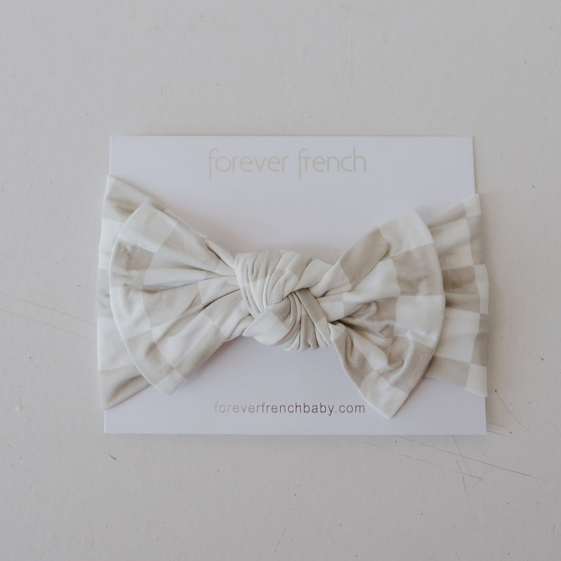 Baby wearing a neutral beige and white checkerboard bamboo head wrap with a small bow