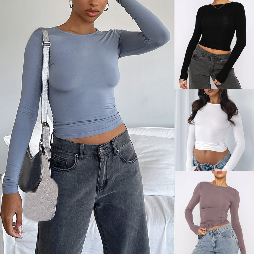 A woman wearing a slim fit long sleeve crop top in dusty blue paired with gray jeans.