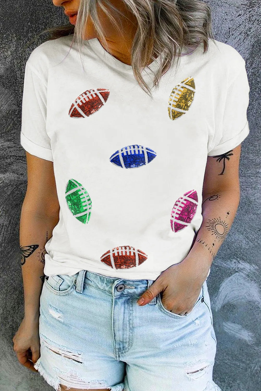 A woman wearing a white short sleeve t-shirt featuring multi-colored sequin football patches.