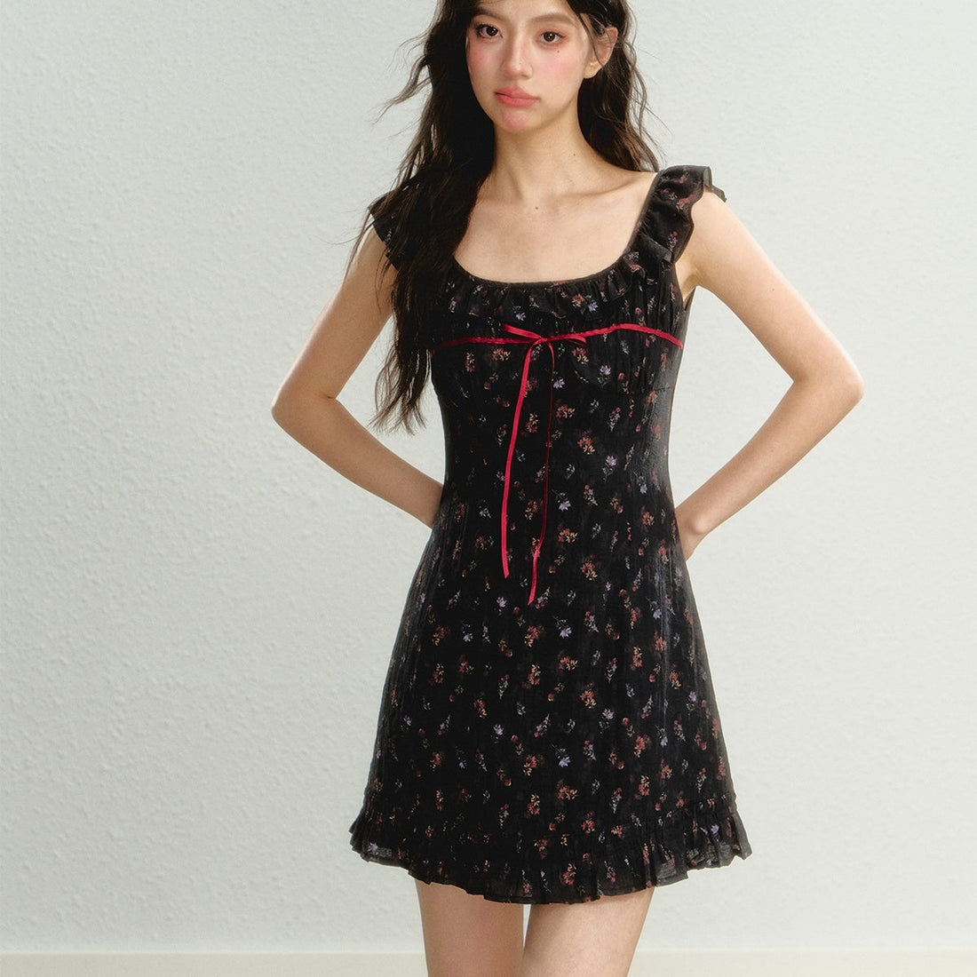 Model wearing a black floral sleeveless mini dress with ruffle straps and a red ribbon detail