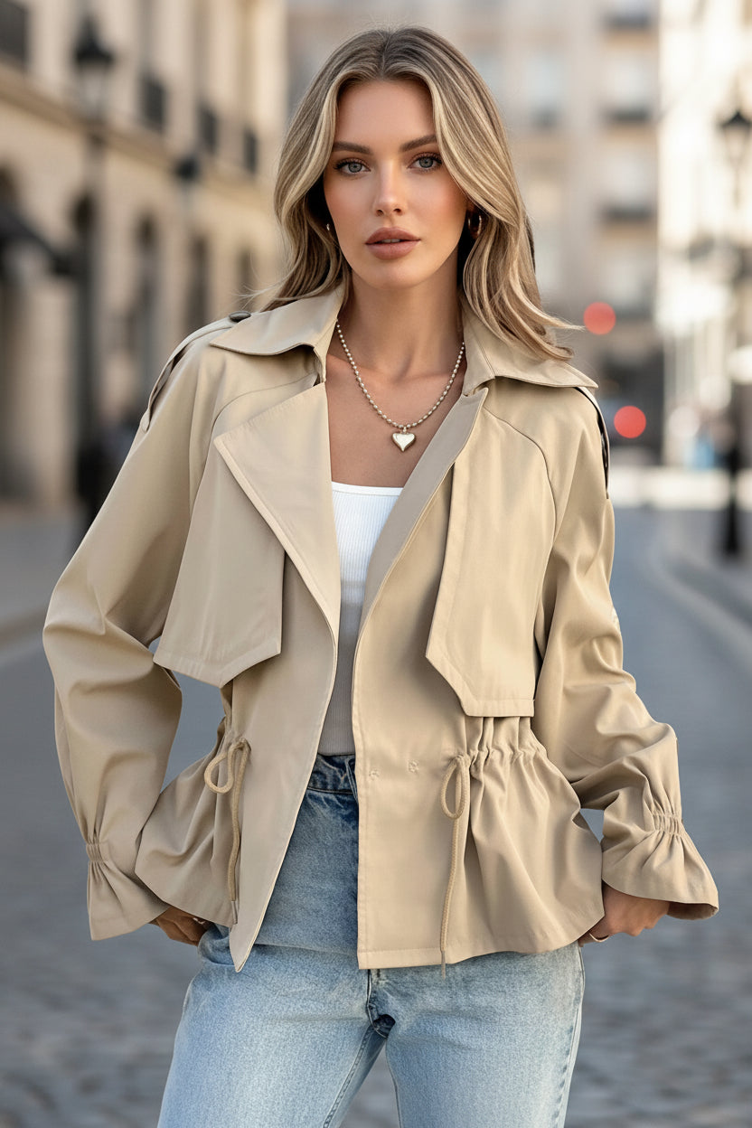 A woman wearing a beige khaki utility coat with an adjustable drawstring waist and lapel collar outdoors.