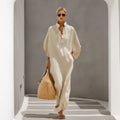 A woman wearing a long-sleeved beige stand collar button-down maxi dress in a minimalist architectural setting.