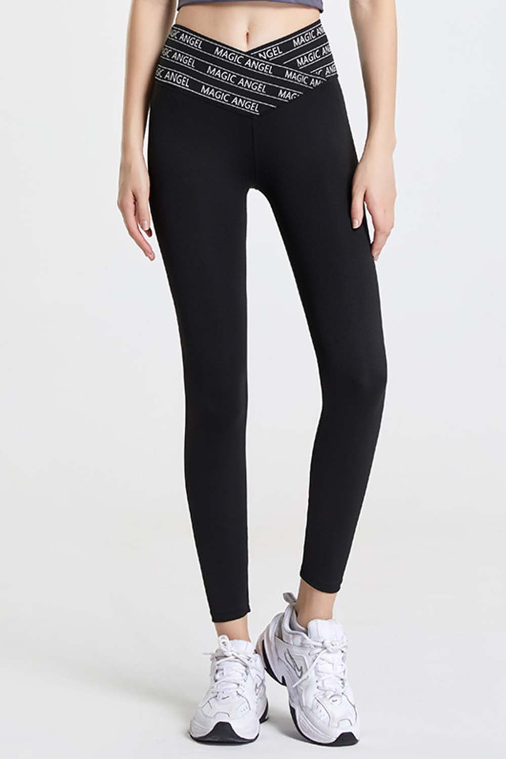 Model wearing black high-waisted sports leggings with Magic Angel slogan on the waistband, paired with white athletic sneakers.