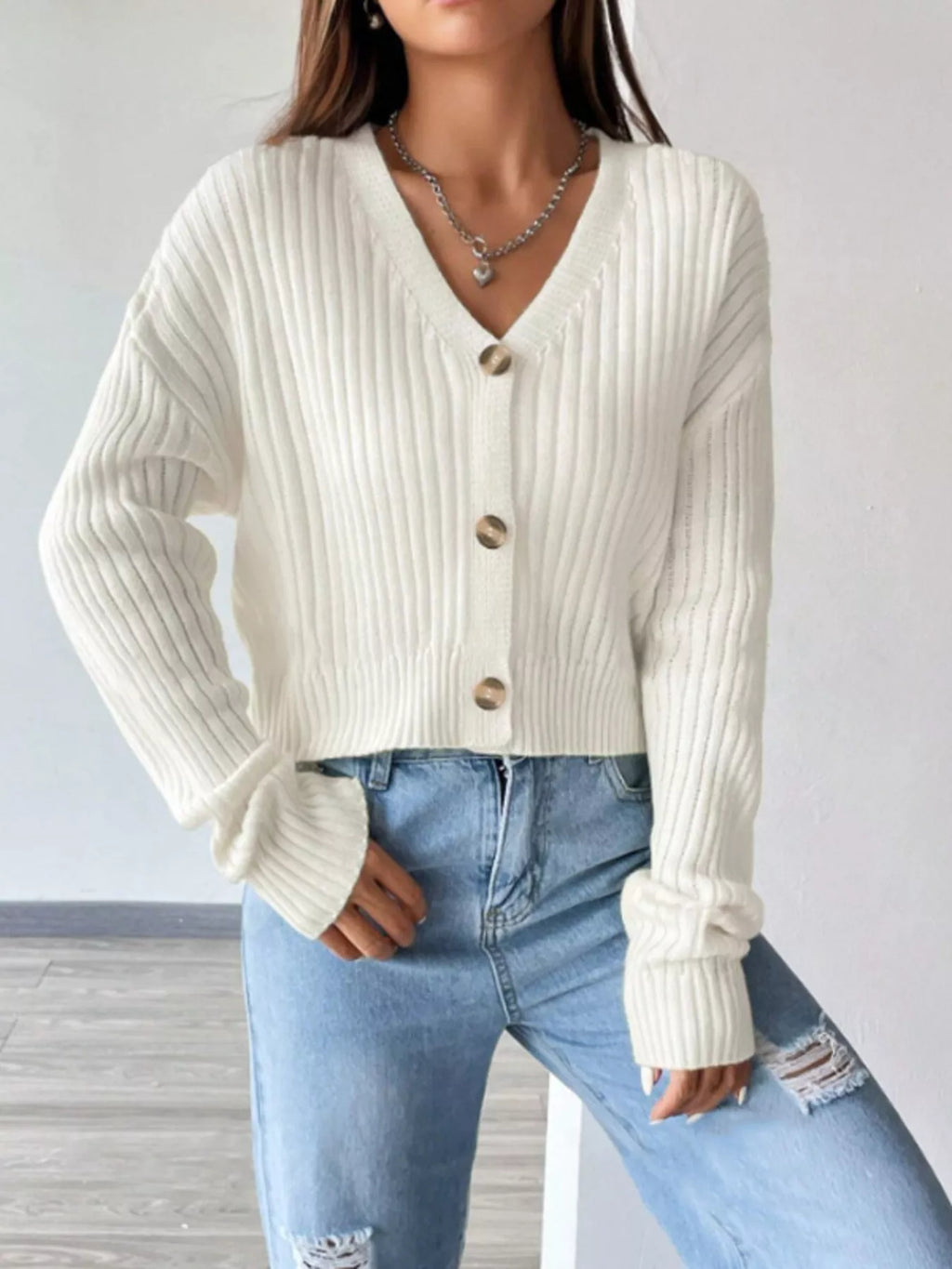 Model wearing a white ribbed V-neck button-up cropped cardigan with light wash distressed denim jeans
