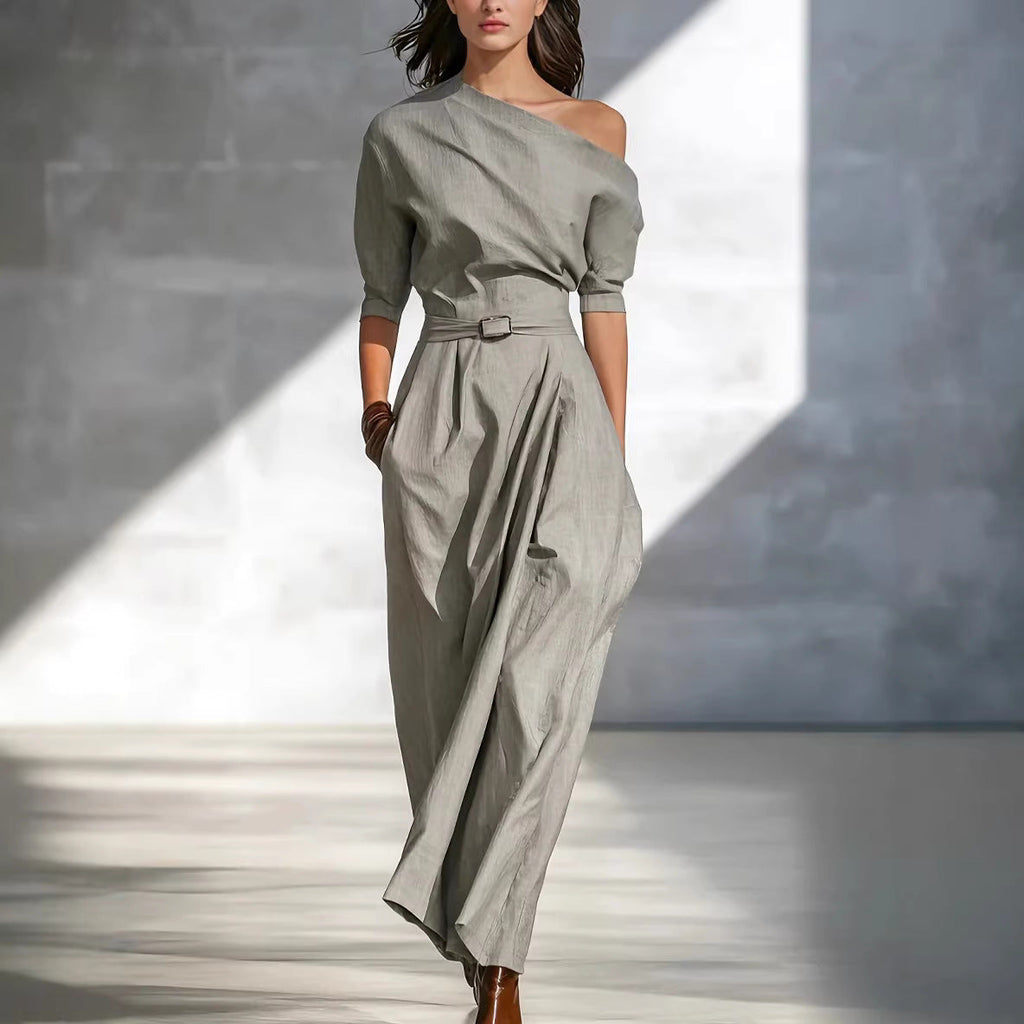 A woman wearing a sage green one-shoulder maxi dress with a belted waist and elbow-length sleeves, walking on a city street.