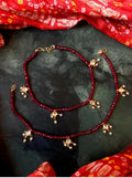A pair of elegant red Kundan and cheer anklets with brass base on a neutral background