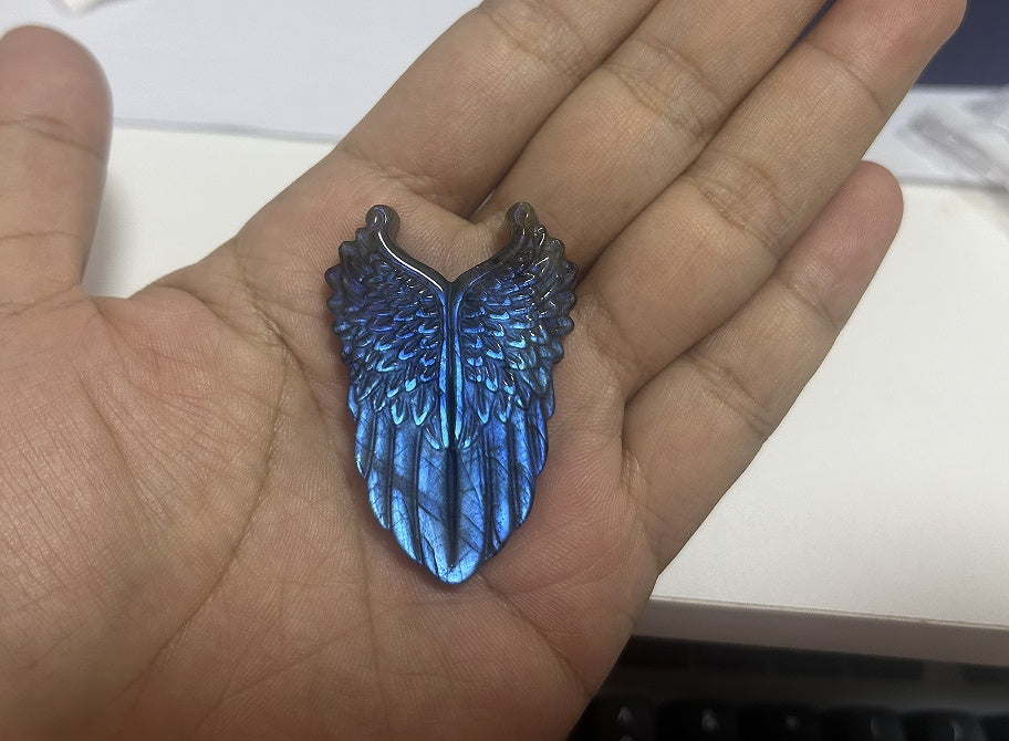 Hand-carved labradorite angel wings pendant with blue iridescent flash set in stainless steel on a light background.