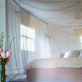 A bedroom featuring a sheer grey EMF protective bed canopy hanging over a bed, with floral decor in the foreground.