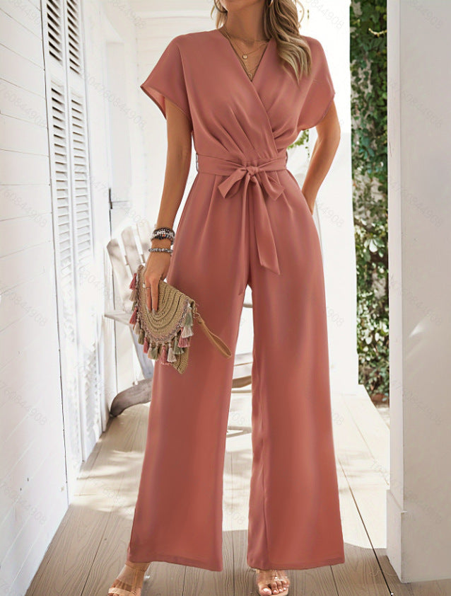 A woman wearing a solid color wide-leg jumpsuit with a V-neck and belted waist in a minimalist casual-chic style.