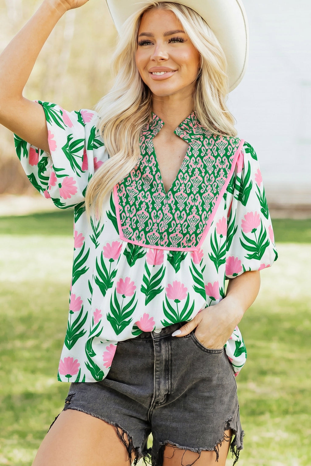 White, green, and pink floral print V-neck blouse with decorative paneling and short sleeves.
