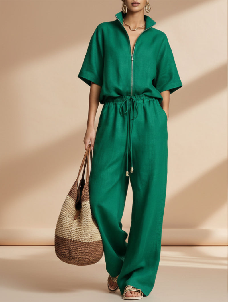 Model wearing a matching emerald green zip-front short sleeve top and wide-leg pants set with a straw bag.