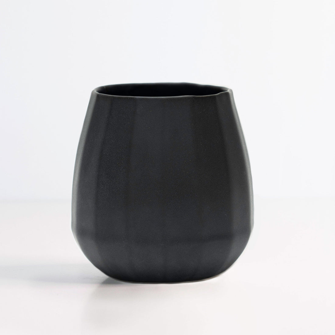 Hand holding a modern matte black ceramic stemless wine glass against a white background