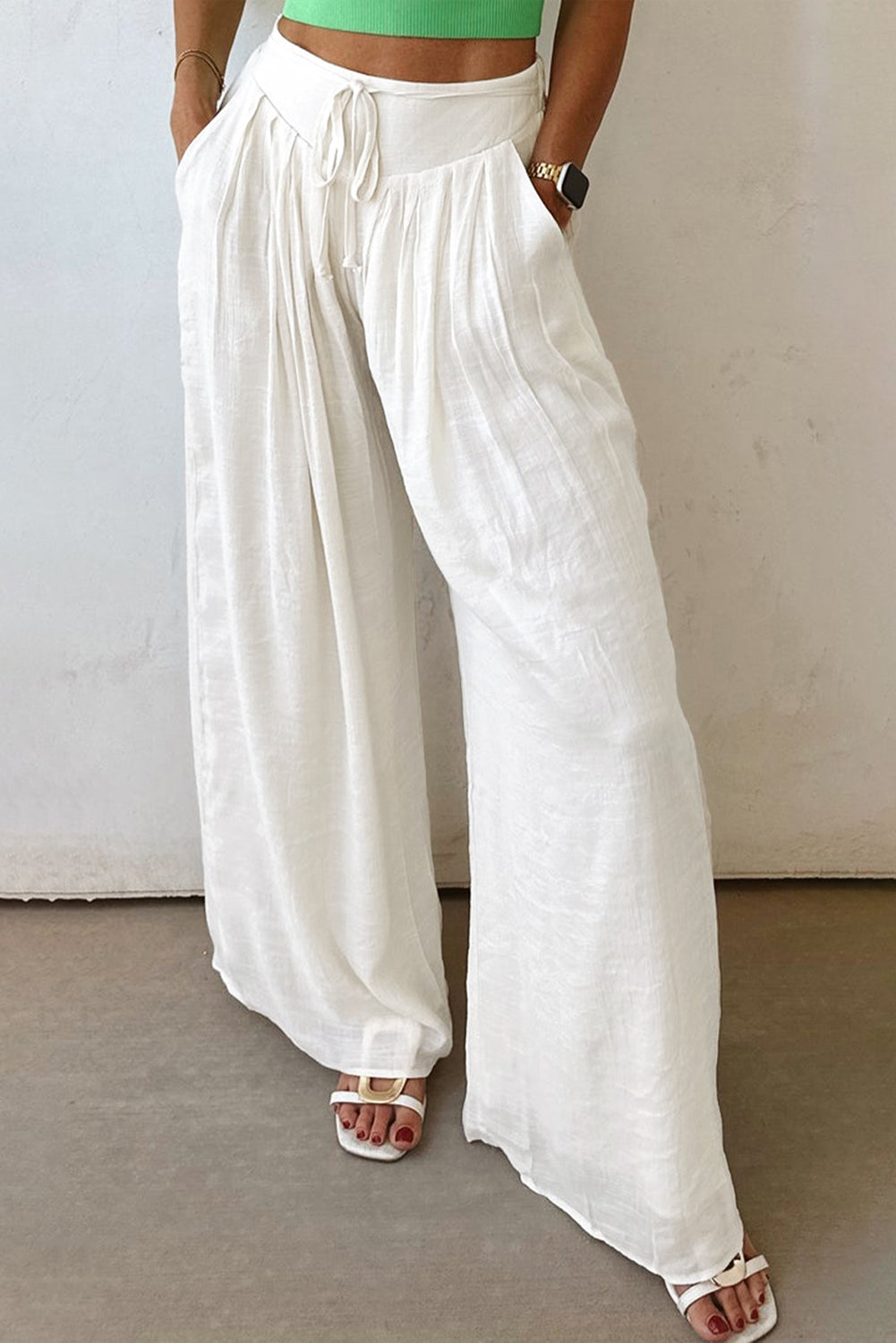 Model wearing white high-waisted wide-leg pleated pants with a drawstring waist detail