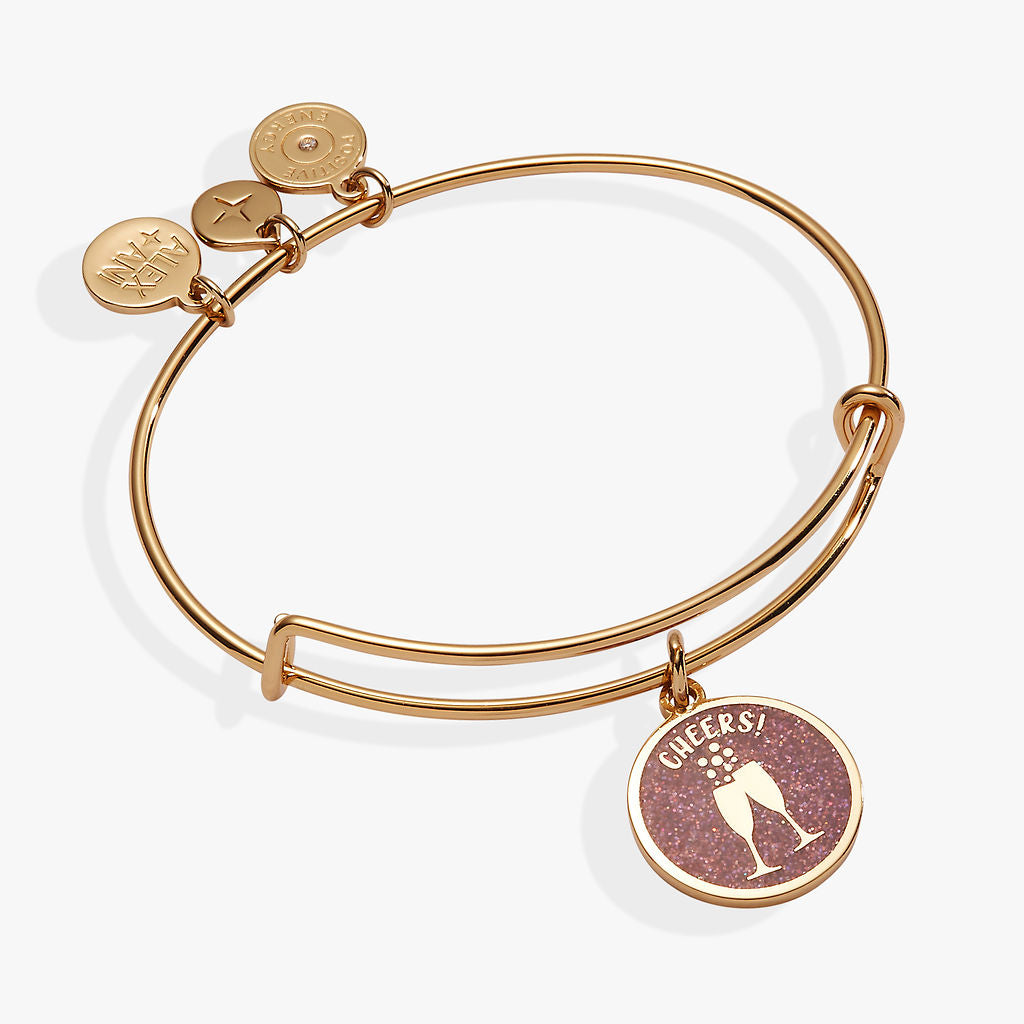 Gold expandable wire bangle featuring a pink glitter champagne glasses charm for New Year's Eve.