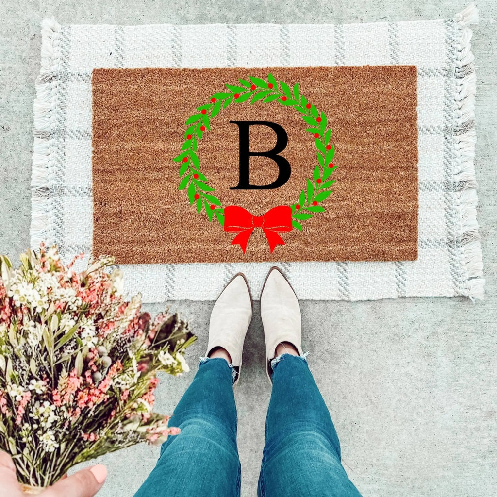 A festive personalized Christmas wreath doormat featuring a custom last initial for holiday entryway decor.